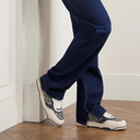 Model sitting wearing beige and blue sneakers styled with dark jeans